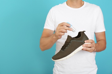 Photo of Man putting capsule shoe freshener in footwear on color background