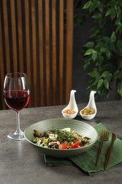 Photo of Tasty dish with tarragon, salad dressings and glass of wine served on grey table