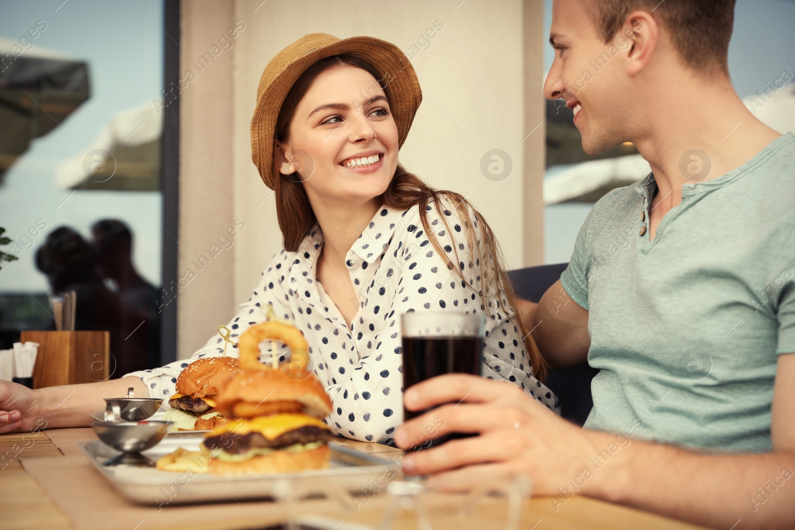 Photo of Young happy couple with burgers in street cafe