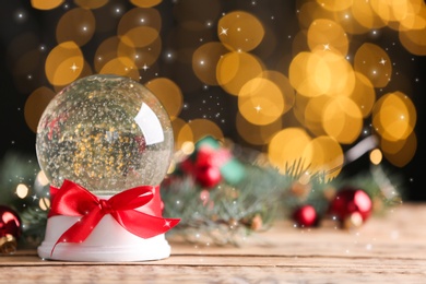 Image of Beautiful snow globe and Christmas decor on wooden table against blurred festive lights, space for text. Bokeh effect