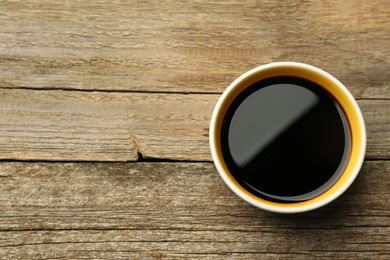 Photo of Soy sauce in bowl on wooden table, top view. Space for text