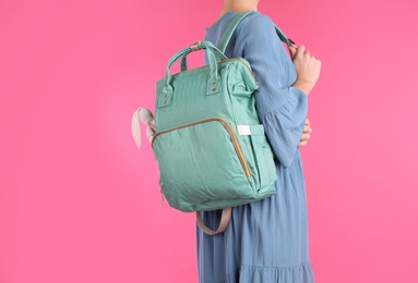 Woman with maternity backpack for baby accessories on color background, closeup