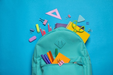 Stylish backpack with different school stationary on blue background, top view