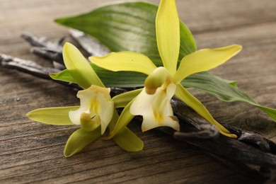 Vanilla pods, beautiful flowers and green leaves on wooden table, closeup