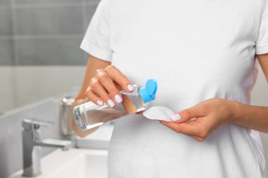 Woman pouring micellar water onto cotton pad in bathroom, closeup