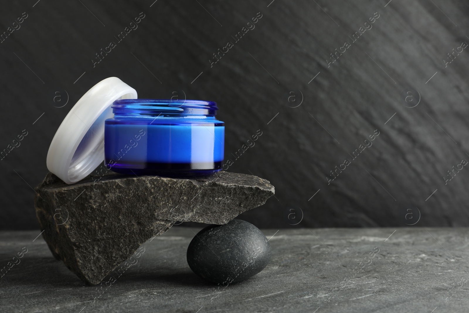 Photo of Jar of cream and stones on grey background. Space for text