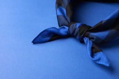 Photo of Tied bandana with check pattern on blue background, closeup