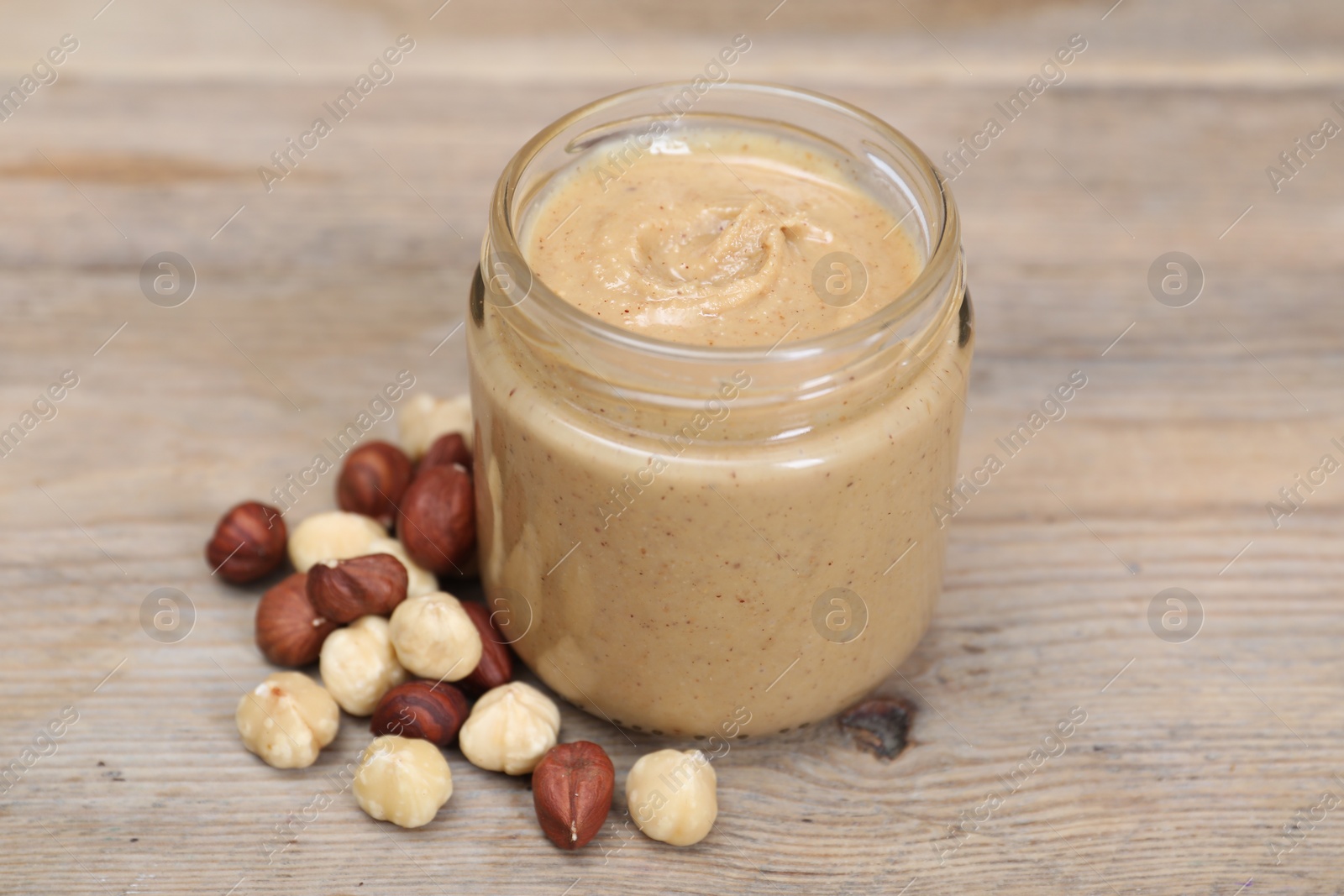 Photo of Tasty nut paste in jar and hazelnuts on wooden table, closeup