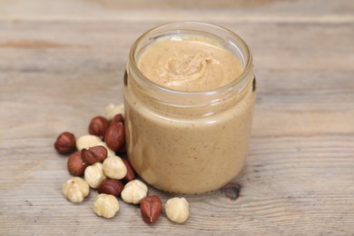 Tasty nut paste in jar and hazelnuts on wooden table, closeup