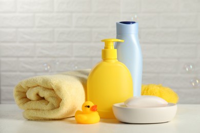 Photo of Baby cosmetic products, bath duck, sponge and towel on white table against soap bubbles