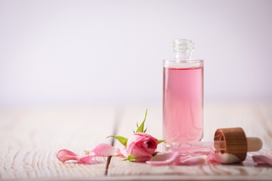 Bottle of essential rose oil and flowers on white wooden table against light background. Space for text