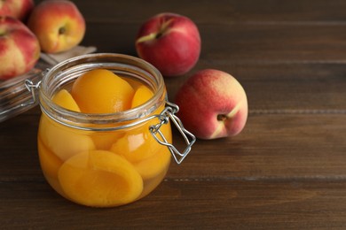 Canned peach halves in glass jar on wooden table, space for text