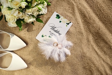 Photo of Flat lay composition with wedding invitation and gold rings on sandy beach
