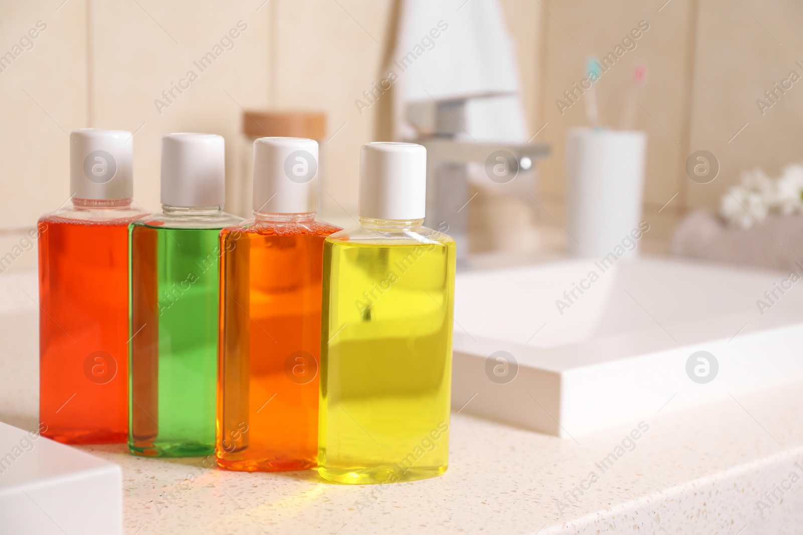 Photo of Fresh mouthwashes in bottles on countertop near sink, closeup. Space for text