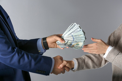 Photo of Man shaking hands with woman and offering bribe on grey background, closeup