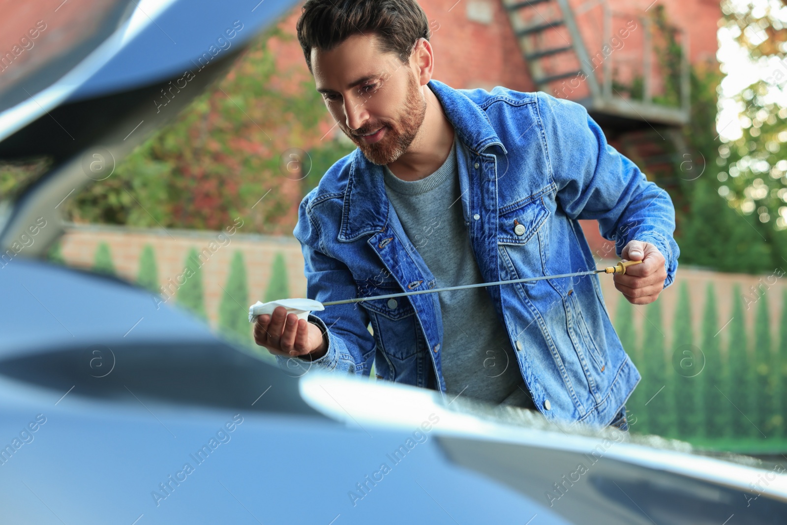 Photo of Man checking motor oil level with dipstick outdoors