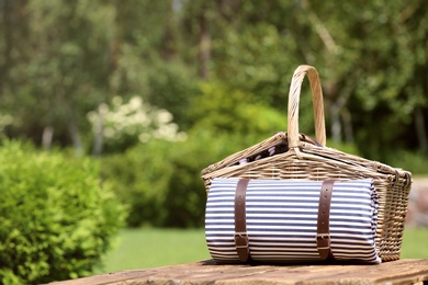 Picnic basket with blanket on wooden table in garden. Space for text