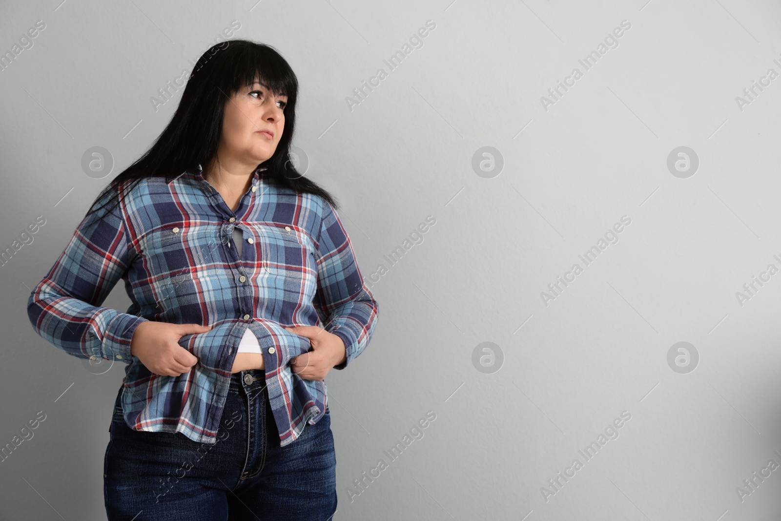 Photo of Overweight woman in tight shirt on light grey background. Space for text