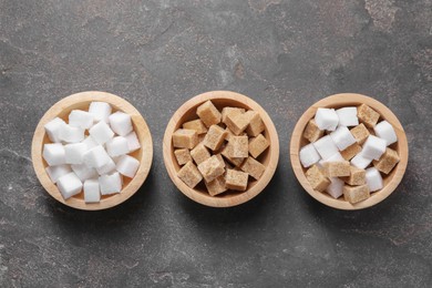 Different sugar cubes in bowls on gray textured table, flat lay