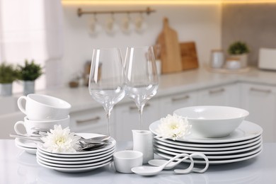 Photo of Set of clean dishware, glasses, cutlery and flowers on table in kitchen