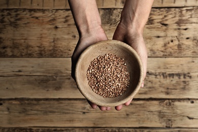 Poor woman holding bowl with grains against wooden background, closeup