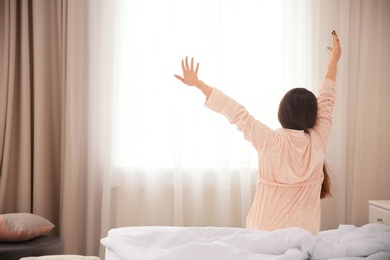 Photo of Young woman stretching on bed in hotel room