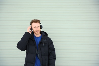 Young man listening to music with headphones against light wall. Space for text