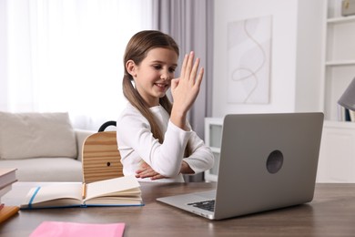 Photo of E-learning. Cute girl raising her hand to answer during online lesson at table indoors