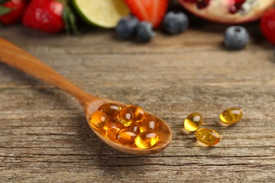 Vitamin pills in spoon and fresh fruits on wooden table