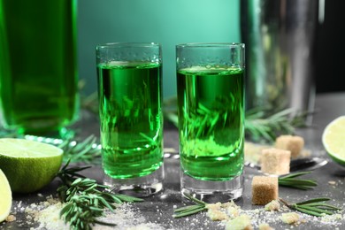 Photo of Absinthe in shot glasses, brown sugar, rosemary and lime on gray table, closeup. Alcoholic drink