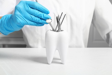 Photo of Dentist putting professional tool into tooth shaped holder at table, closeup