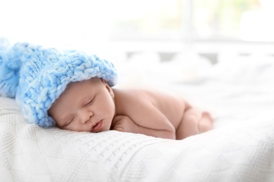 Photo of Adorable newborn baby in large knitted hat lying on bed against light background