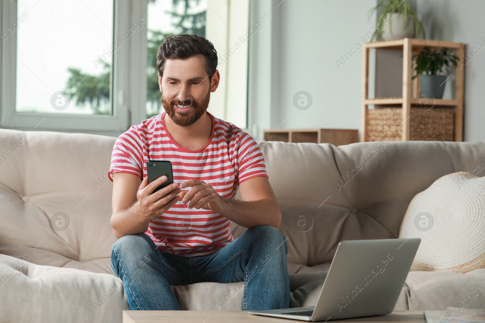 Photo of Handsome man using smartphone on sofa at home