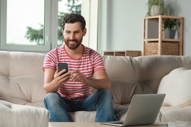 Photo of Handsome man using smartphone on sofa at home