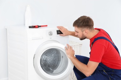 Young plumber examining washing machine in bathroom