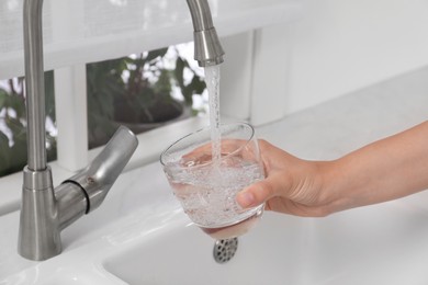 Woman filling glass with water from tap at home, closeup