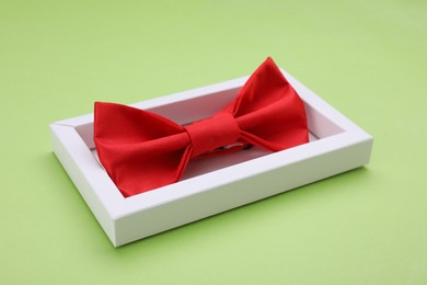 Photo of Stylish red bow tie in box on light green background