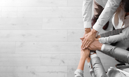 Photo of People holding hands together over light wooden background, top view with space for text. Unity concept