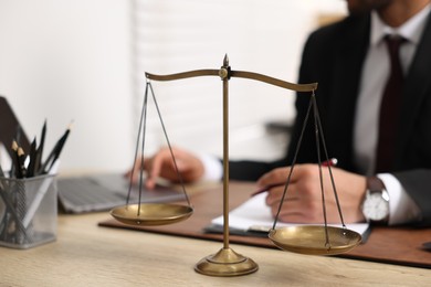 Lawyer working at table in office, focus on scales of justice