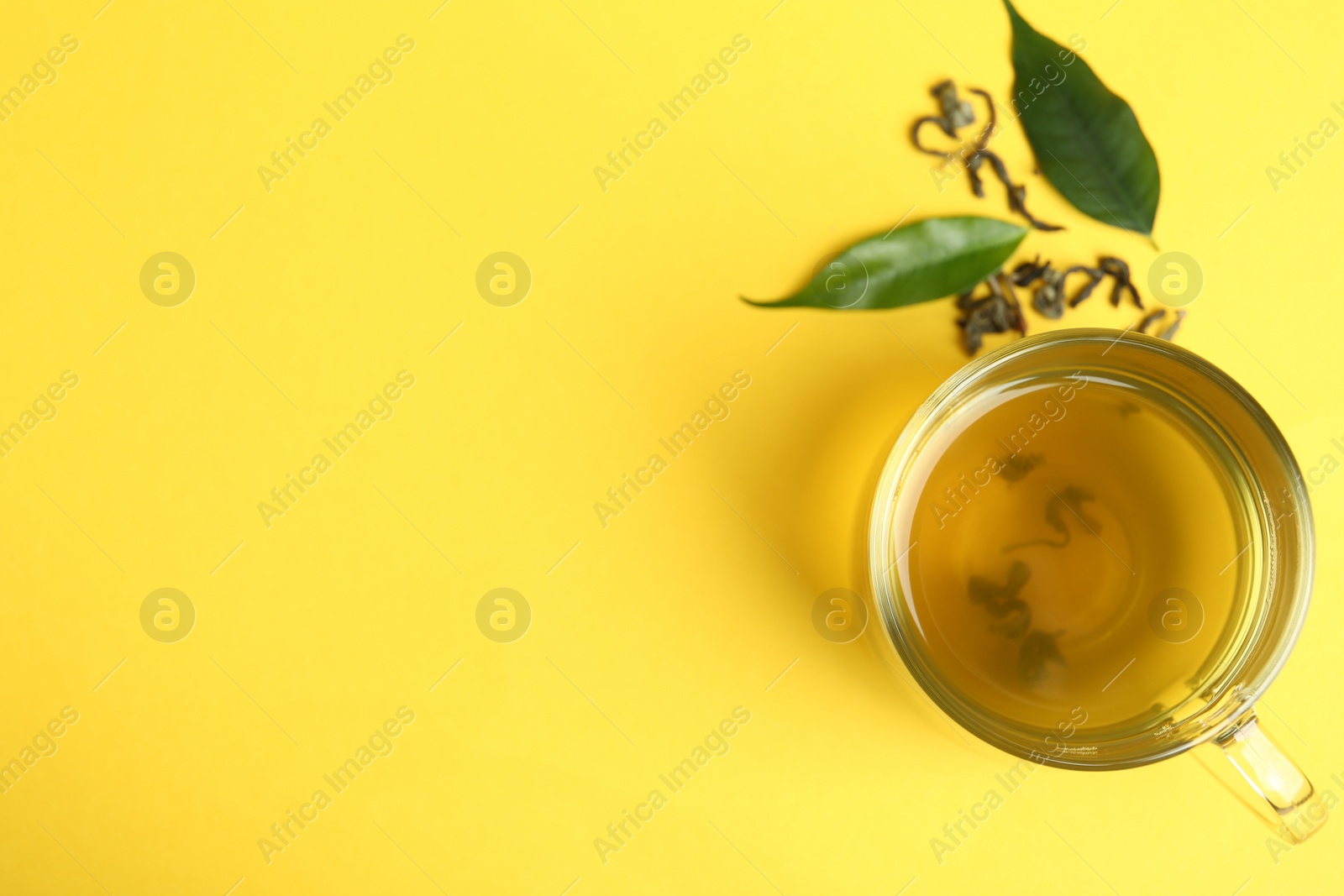 Photo of Cup of green tea and leaves on yellow background, flat lay. Space for text