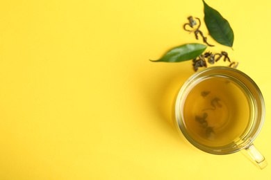 Cup of green tea and leaves on yellow background, flat lay. Space for text