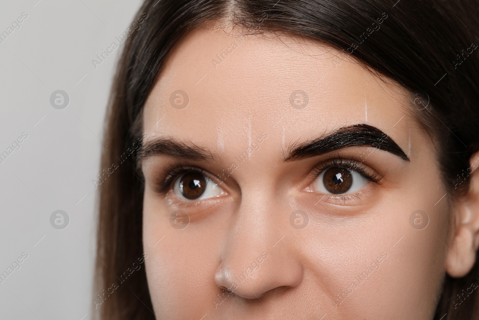 Photo of Woman during eyebrow tinting procedure on grey background, closeup