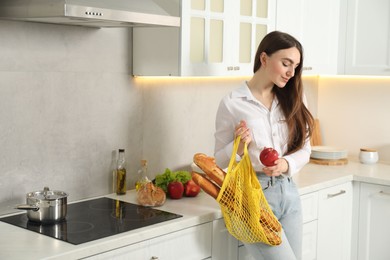 Photo of Woman with string bag of baguettes and apple in kitchen