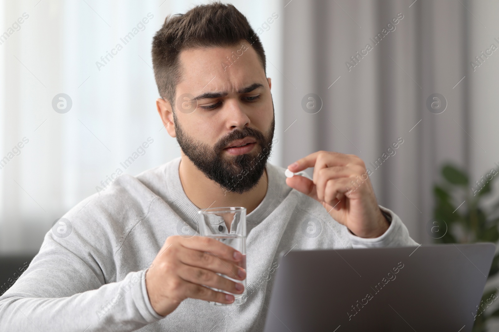 Photo of Young man taking pill against headache in office