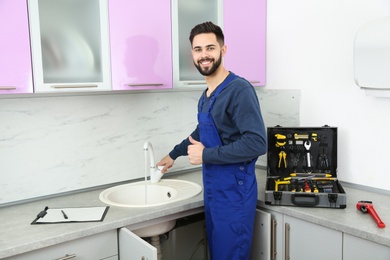 Photo of Male plumber in uniform checking faucet in kitchen. Repair service