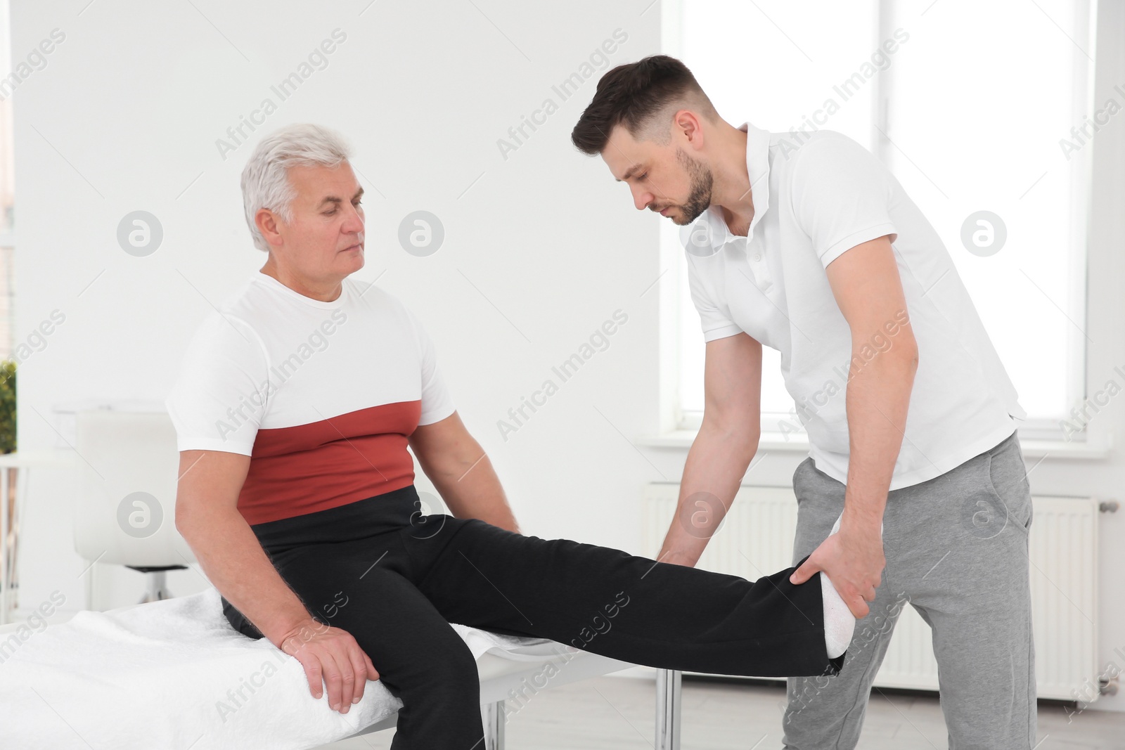 Photo of Young physiotherapist working with senior patient in clinic