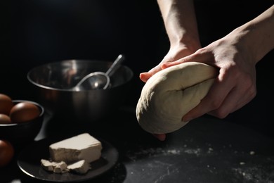 Making bread. Woman kneading dough at black table on dark background, closeup. Space for text