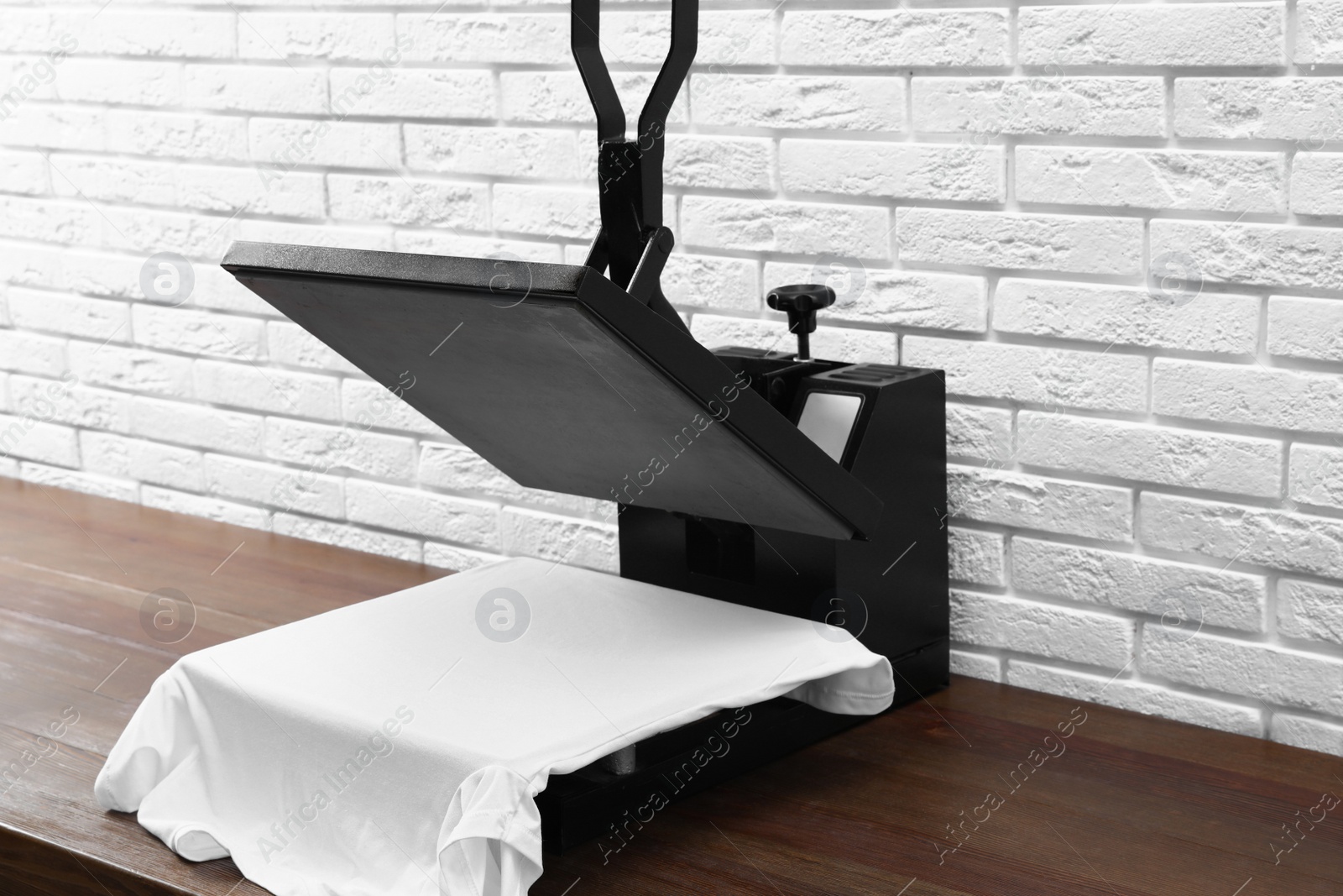 Photo of Heat press machine with t-shirt on wooden table near white brick wall