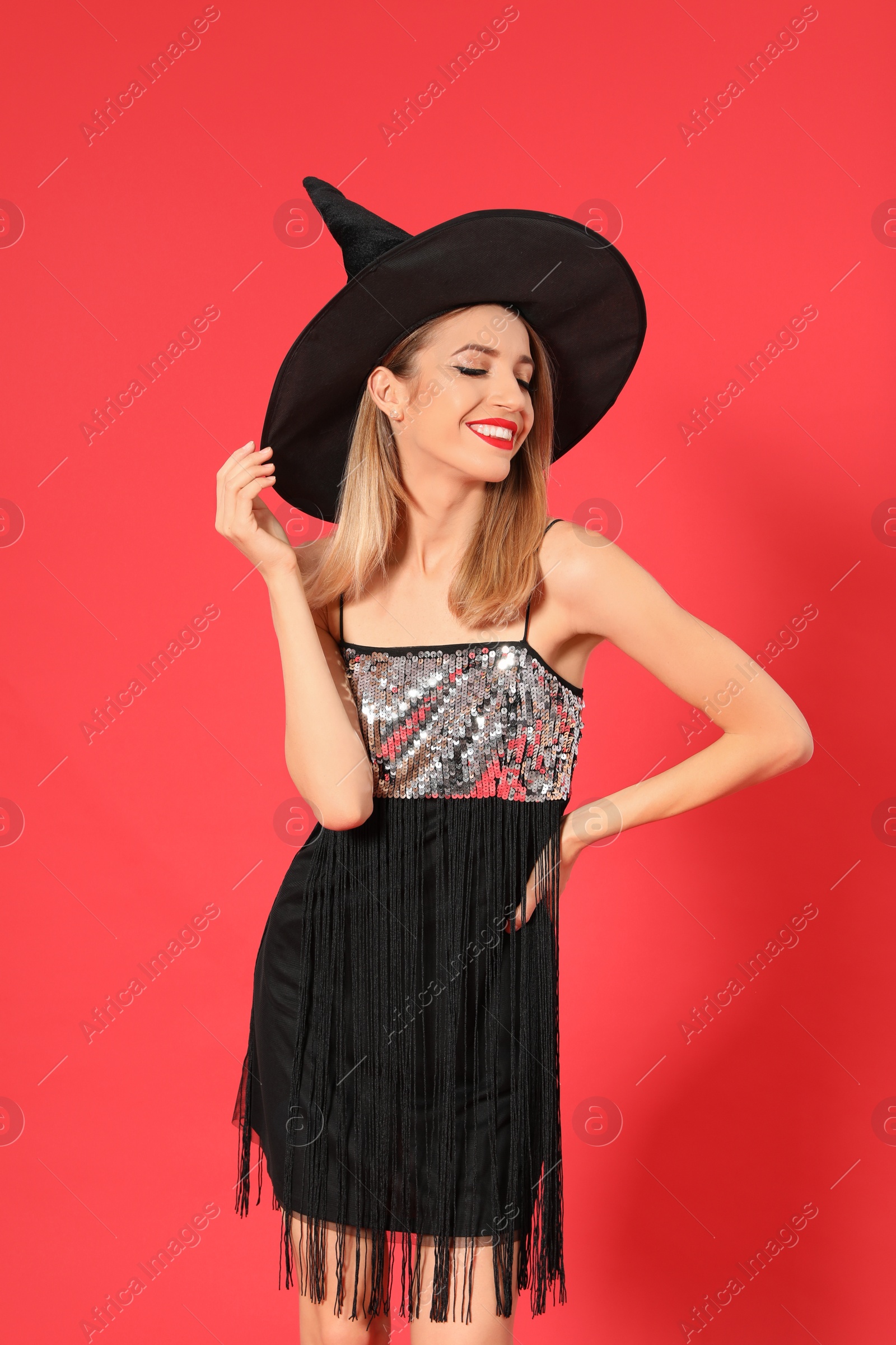 Photo of Beautiful young woman wearing witch costume for Halloween party on red background