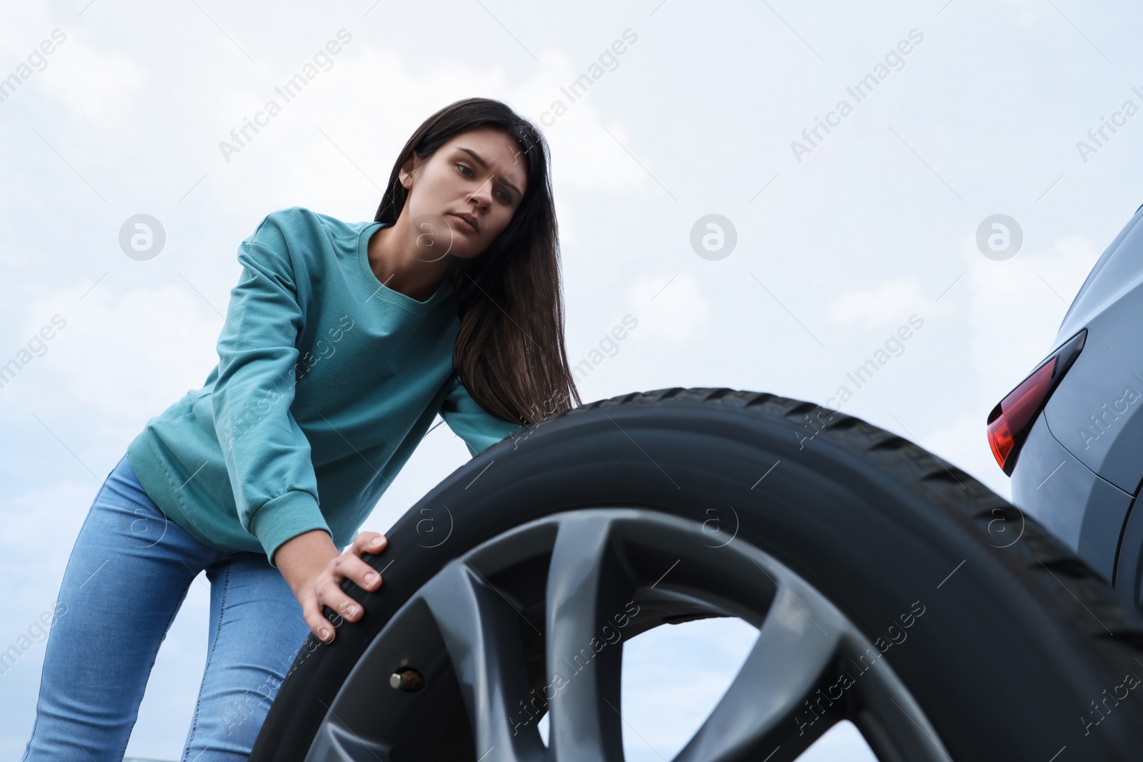 Photo of Young woman changing tire of car on roadside